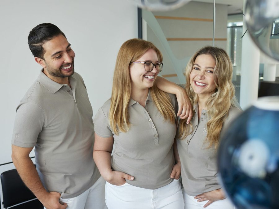 Drei Teammitglieder lachen sich an und lehnen sich aneinander